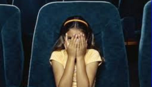 Girl covering her eyes in movie theater seat